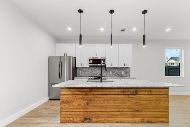 kitchen with light wood finished floors, stainless steel appliances, tasteful backsplash, white cabinets, and an island with sink