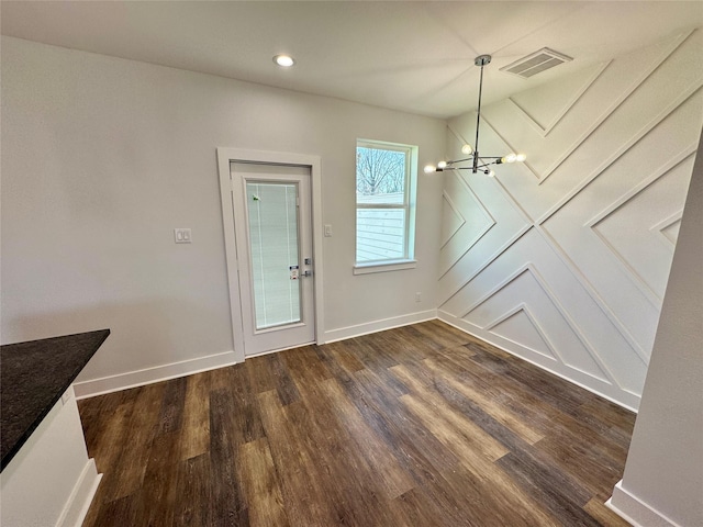 unfurnished dining area with dark wood-style floors, a chandelier, visible vents, and baseboards