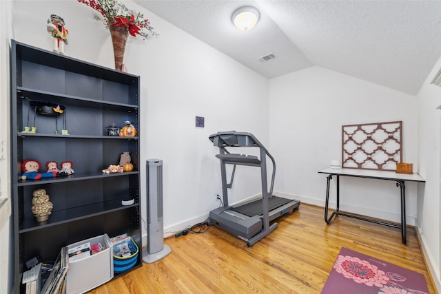 exercise room featuring lofted ceiling, light wood-style floors, visible vents, and a textured ceiling