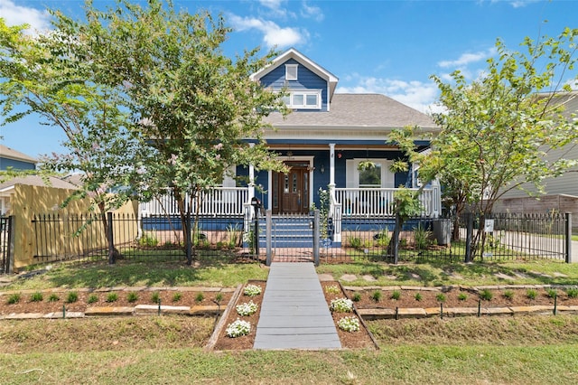 view of front facade with covered porch, a shingled roof, and a fenced front yard