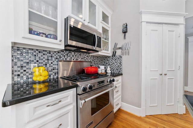 kitchen with stainless steel appliances, dark countertops, light wood finished floors, and tasteful backsplash