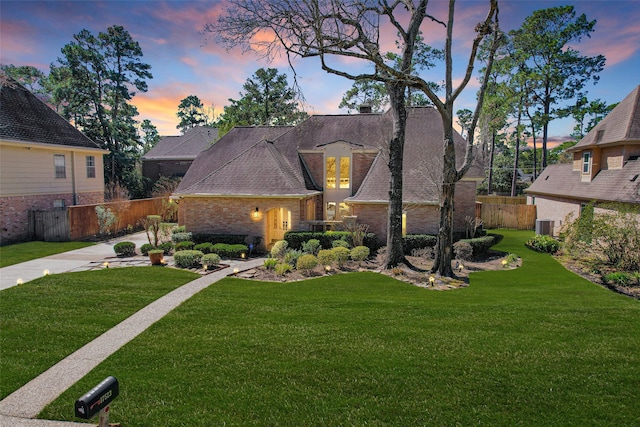 view of front of home featuring roof with shingles, brick siding, central AC unit, fence, and a front lawn