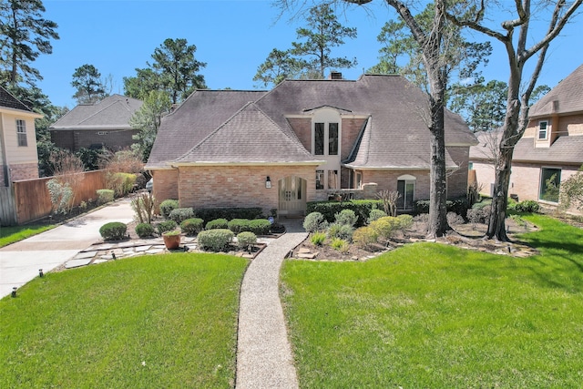 french provincial home with fence, a front lawn, and brick siding