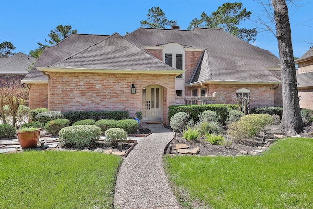 french provincial home featuring brick siding, roof with shingles, and a front yard