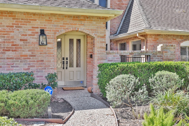 doorway to property featuring a shingled roof and brick siding