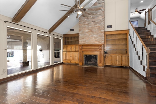 unfurnished living room with ceiling fan, a large fireplace, dark wood-style flooring, stairs, and beamed ceiling