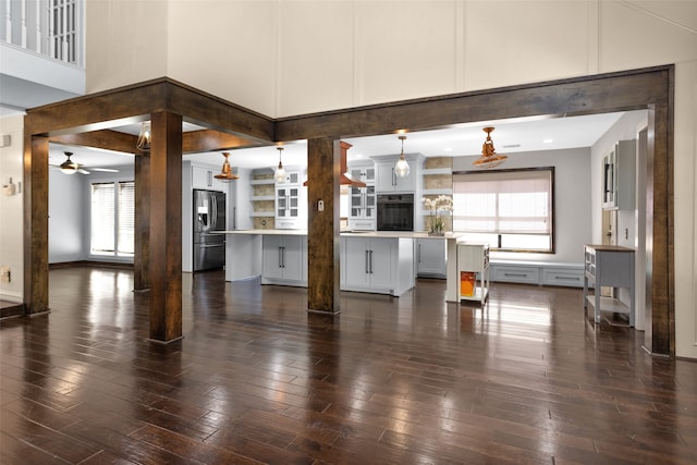 unfurnished living room with decorative columns, dark wood finished floors, a towering ceiling, and a ceiling fan