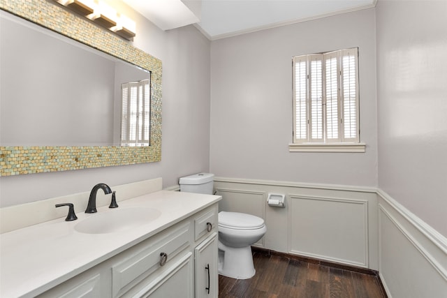 bathroom with toilet, wood finished floors, vanity, wainscoting, and crown molding