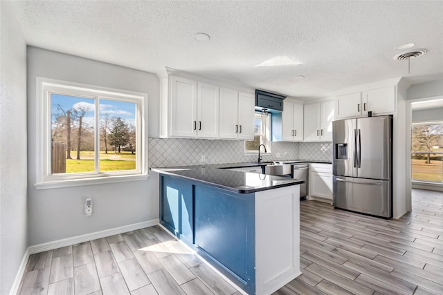 kitchen with tasteful backsplash, white cabinets, dark countertops, a peninsula, and stainless steel appliances