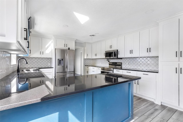 kitchen featuring stainless steel appliances, a peninsula, decorative backsplash, and white cabinets