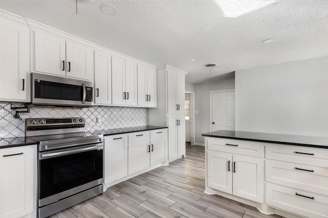 kitchen featuring dark countertops, visible vents, decorative backsplash, appliances with stainless steel finishes, and white cabinets