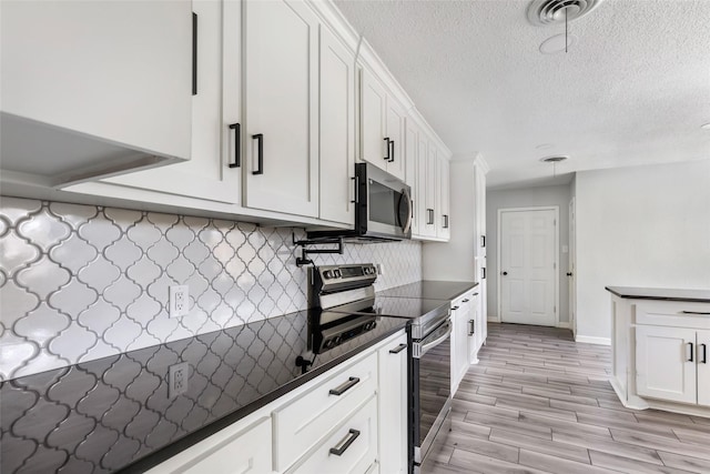 kitchen with tasteful backsplash, dark countertops, visible vents, appliances with stainless steel finishes, and white cabinetry