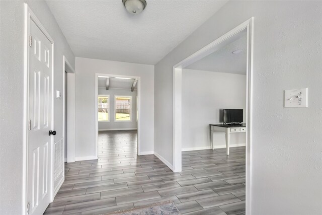 corridor featuring baseboards, a textured ceiling, and wood finish floors