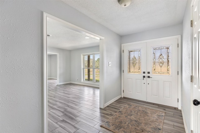 entryway with a textured ceiling, a textured wall, baseboards, french doors, and wood tiled floor