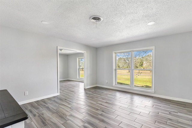 unfurnished room featuring wood finish floors, plenty of natural light, visible vents, and baseboards