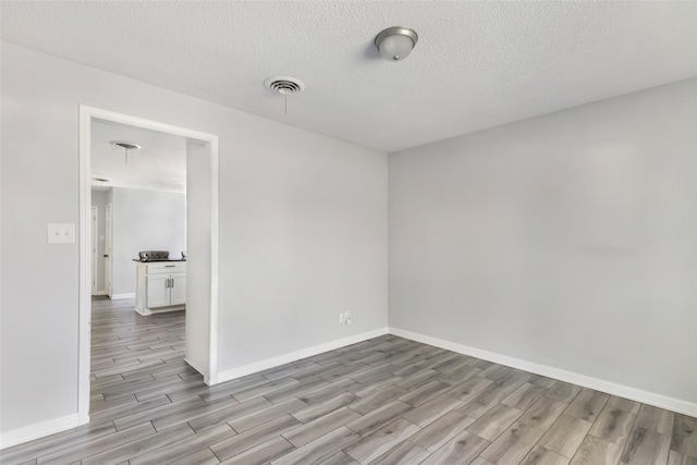 unfurnished room featuring visible vents, a textured ceiling, light wood-style flooring, and baseboards