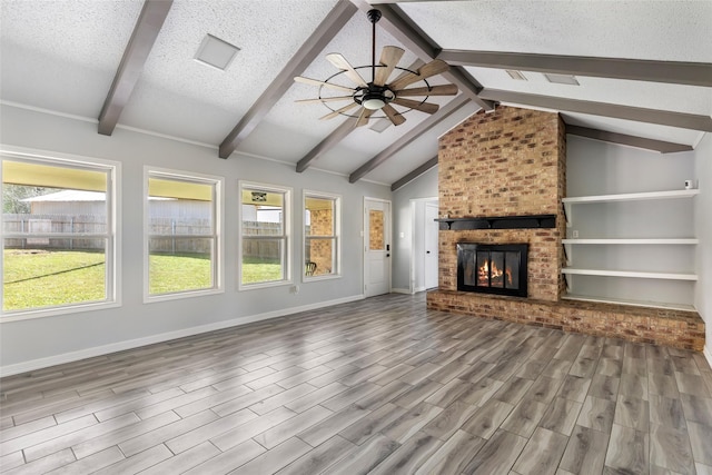 unfurnished living room with a textured ceiling, ceiling fan, lofted ceiling with beams, a fireplace, and wood finished floors