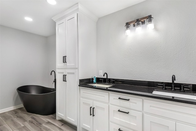 bathroom featuring a soaking tub, double vanity, a sink, and wood finished floors