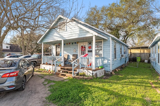 view of front of house with covered porch, a front yard, fence, and cooling unit