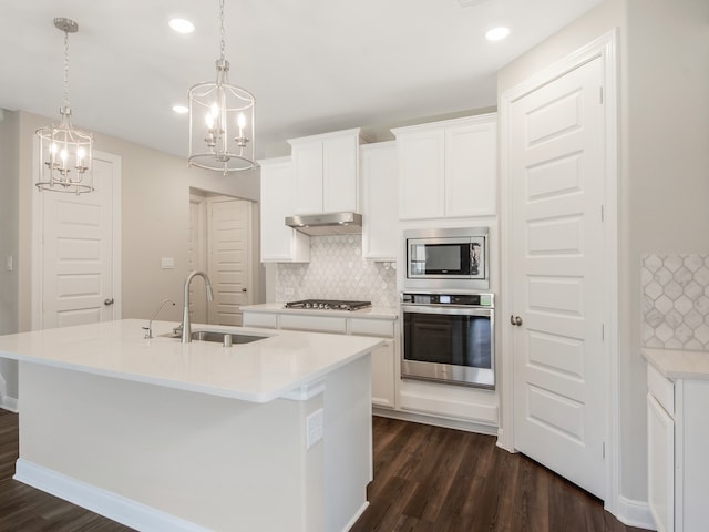 kitchen featuring a kitchen island with sink, under cabinet range hood, a sink, appliances with stainless steel finishes, and dark wood-style floors