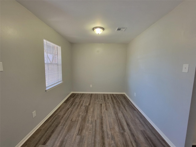 empty room with dark wood-type flooring, visible vents, and baseboards