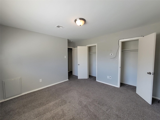 unfurnished bedroom with baseboards, visible vents, dark carpet, and multiple closets