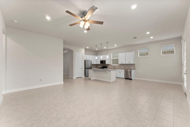 kitchen with arched walkways, a center island, stainless steel appliances, open floor plan, and white cabinets