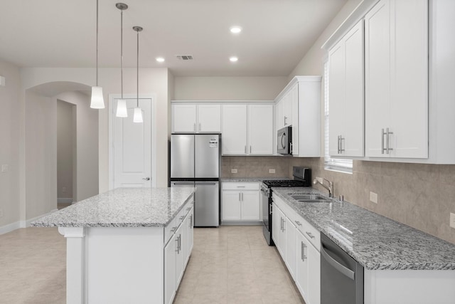 kitchen with arched walkways, stainless steel appliances, a kitchen island, a sink, and visible vents