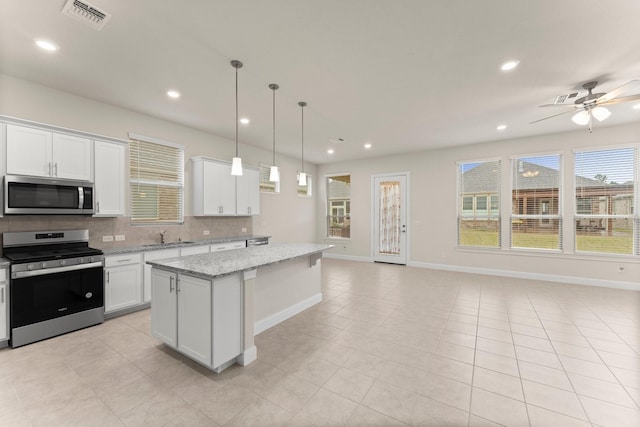 kitchen with stainless steel appliances, a kitchen island, visible vents, white cabinetry, and backsplash