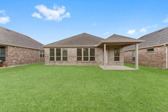 back of property with a yard, a shingled roof, a patio area, and brick siding