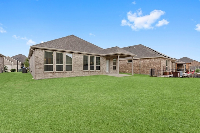 rear view of property featuring brick siding, roof with shingles, fence, and a yard