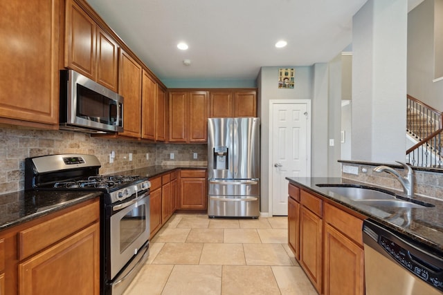 kitchen with stainless steel appliances, dark stone countertops, a sink, and decorative backsplash