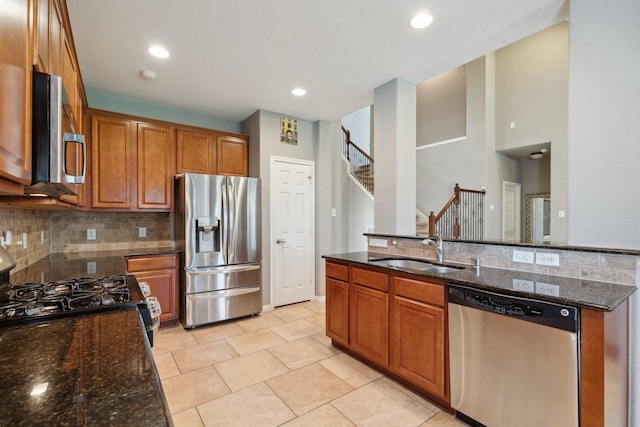 kitchen with brown cabinetry, appliances with stainless steel finishes, dark stone countertops, a sink, and backsplash