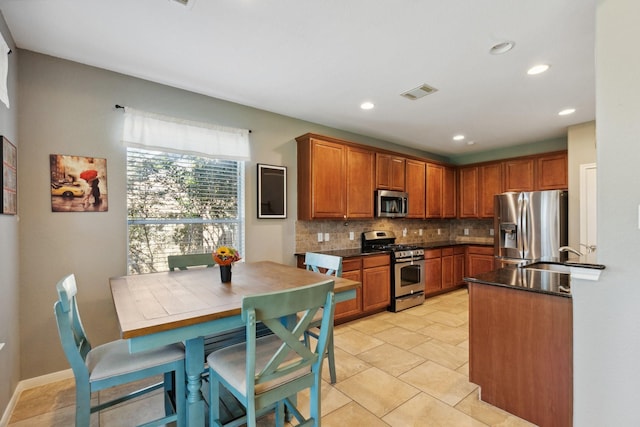 kitchen featuring stainless steel appliances, dark countertops, visible vents, backsplash, and a sink