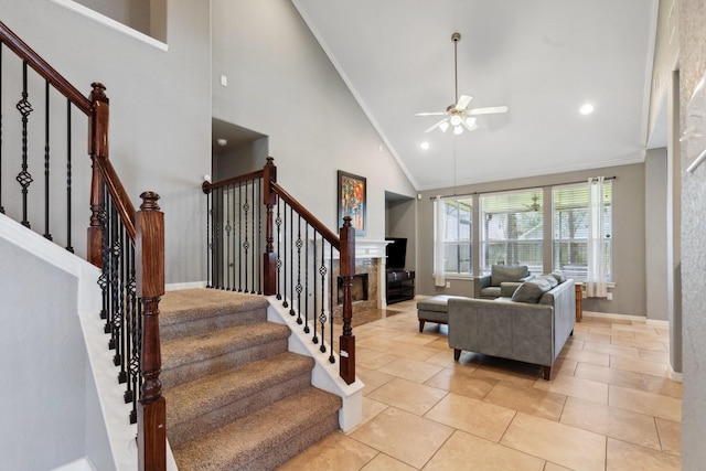 living area with ceiling fan, light tile patterned flooring, a fireplace, stairs, and crown molding