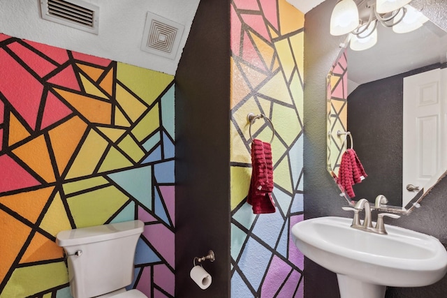 half bath featuring a textured wall, visible vents, a sink, and toilet