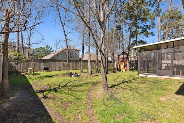 view of yard featuring a playground, a fenced backyard, and a sunroom