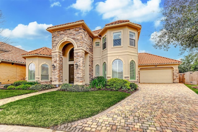 mediterranean / spanish house with stone siding, an attached garage, fence, a front yard, and stucco siding