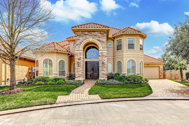 mediterranean / spanish-style house featuring stone siding, stucco siding, an attached garage, decorative driveway, and a front yard