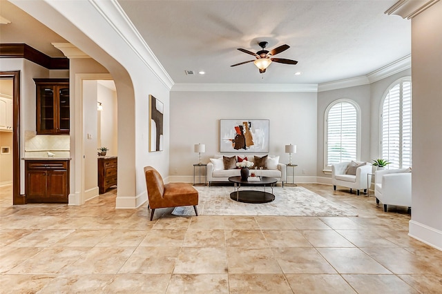 living area featuring arched walkways, light tile patterned floors, ornamental molding, a ceiling fan, and baseboards