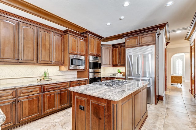 kitchen featuring arched walkways, a kitchen island, light stone counters, built in appliances, and backsplash