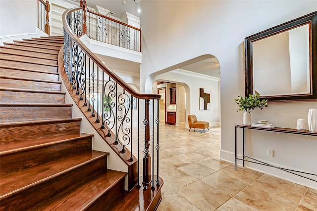 stairs featuring arched walkways, a high ceiling, baseboards, ornamental molding, and tile patterned floors