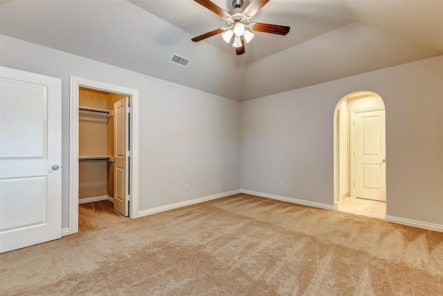 unfurnished bedroom featuring arched walkways, a walk in closet, visible vents, and light colored carpet