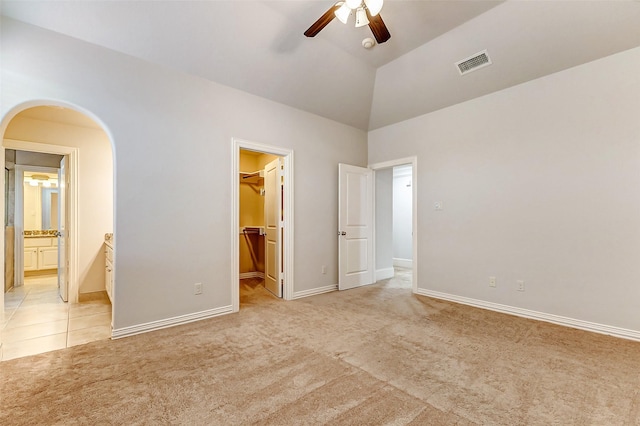 unfurnished bedroom featuring light carpet, visible vents, arched walkways, vaulted ceiling, and a walk in closet