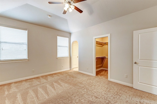 unfurnished bedroom with ceiling fan, baseboards, vaulted ceiling, carpet, and a walk in closet