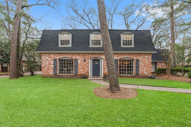 view of front property featuring a shingled roof, mansard roof, a front yard, and brick siding