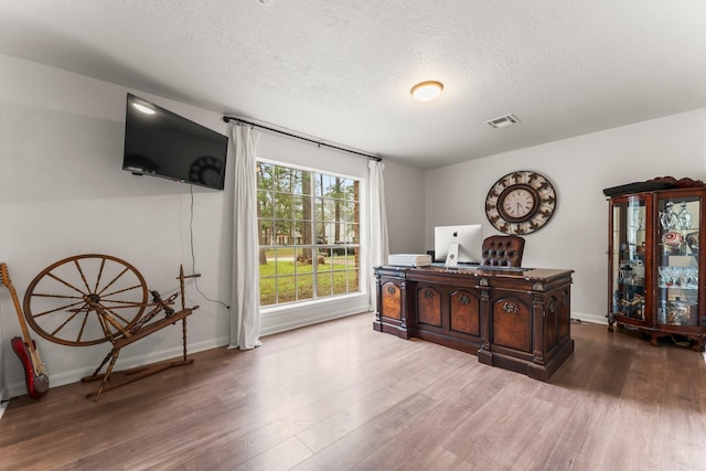 interior space with baseboards, a textured ceiling, visible vents, and wood finished floors