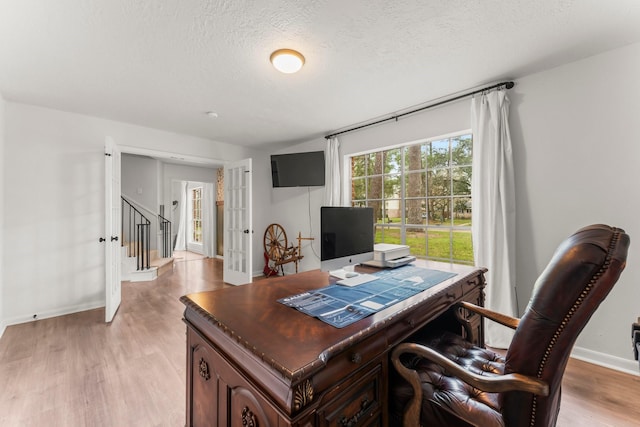 office area featuring light wood finished floors, baseboards, a textured ceiling, and french doors