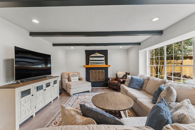 living room featuring a textured ceiling, recessed lighting, a fireplace, light wood finished floors, and beamed ceiling