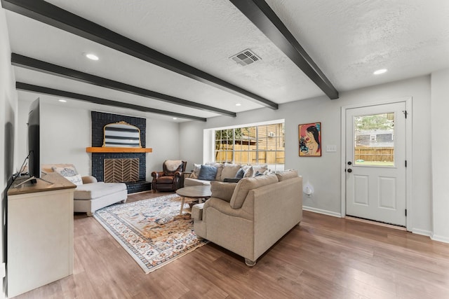 living area featuring visible vents, beamed ceiling, a textured ceiling, and wood finished floors